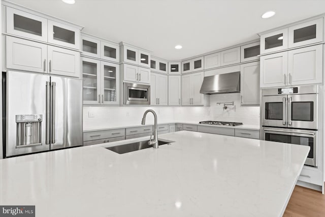 kitchen featuring appliances with stainless steel finishes, light stone counters, wall chimney exhaust hood, and sink