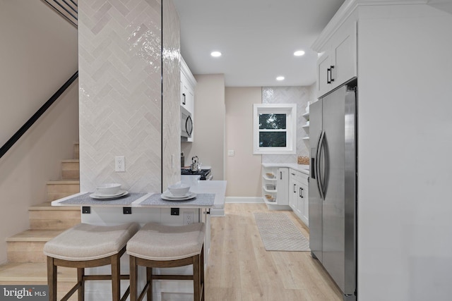 kitchen featuring decorative backsplash, a kitchen breakfast bar, light wood-type flooring, stainless steel appliances, and white cabinetry