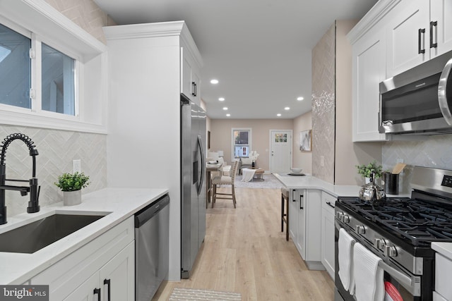 kitchen with light stone countertops, sink, light hardwood / wood-style floors, white cabinets, and appliances with stainless steel finishes