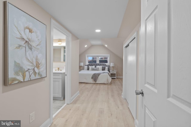 bedroom featuring light wood-type flooring, vaulted ceiling, and connected bathroom