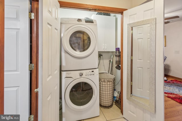 laundry area featuring stacked washer / drying machine, cabinets, and light tile patterned floors