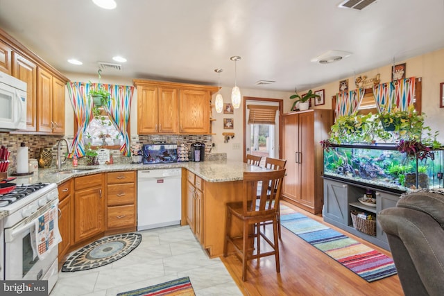 kitchen featuring kitchen peninsula, a breakfast bar, white appliances, light hardwood / wood-style flooring, and hanging light fixtures