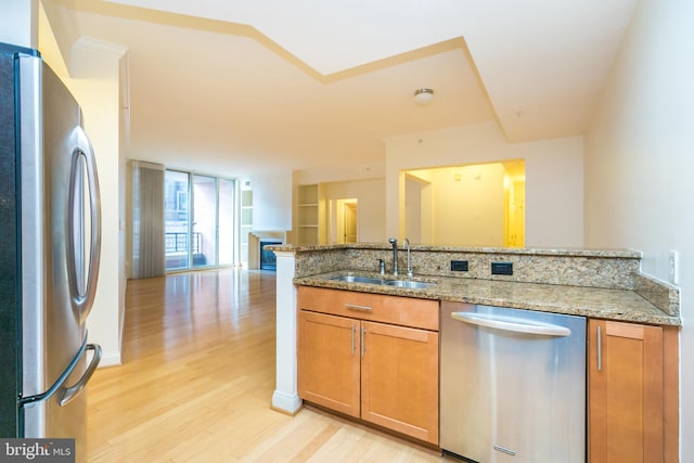 kitchen featuring light stone countertops, kitchen peninsula, stainless steel appliances, sink, and light hardwood / wood-style floors