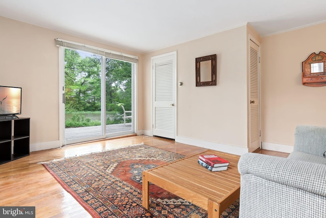 living area featuring ornamental molding, light wood-style flooring, and baseboards