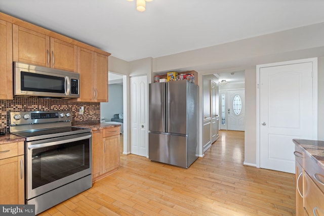 kitchen with decorative backsplash, light hardwood / wood-style flooring, dark stone counters, and appliances with stainless steel finishes