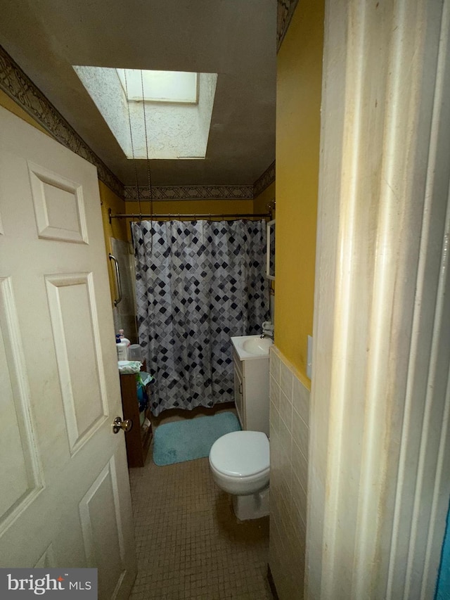 bathroom with a skylight, toilet, tile walls, and curtained shower