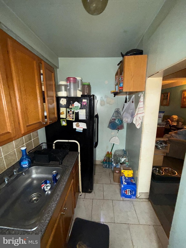 kitchen with backsplash, black refrigerator, sink, and light tile patterned flooring