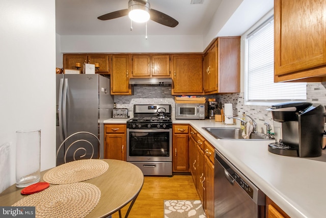 kitchen with backsplash, stainless steel appliances, ceiling fan, sink, and light hardwood / wood-style flooring