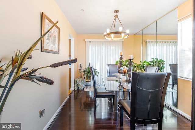 dining area with dark wood-type flooring and an inviting chandelier