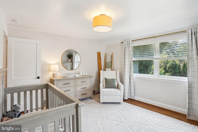 bedroom with light wood-type flooring and a nursery area