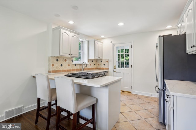 kitchen with stainless steel refrigerator, kitchen peninsula, a kitchen bar, decorative backsplash, and white cabinets