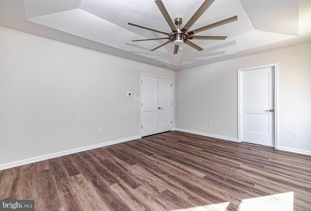 spare room with ceiling fan, a raised ceiling, and dark wood-type flooring