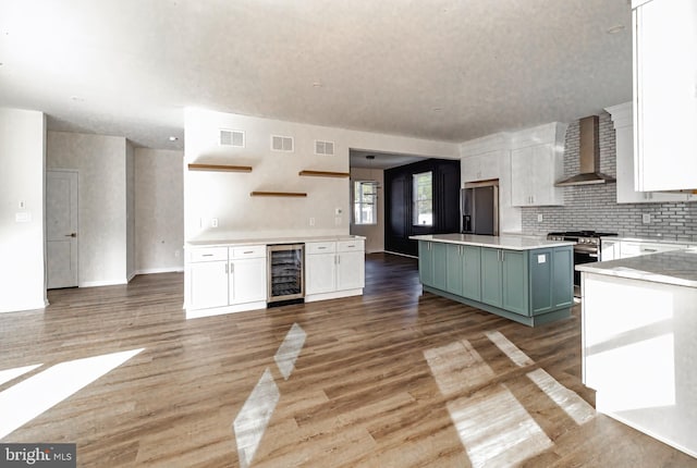 kitchen featuring a center island, green cabinets, wall chimney range hood, wine cooler, and appliances with stainless steel finishes