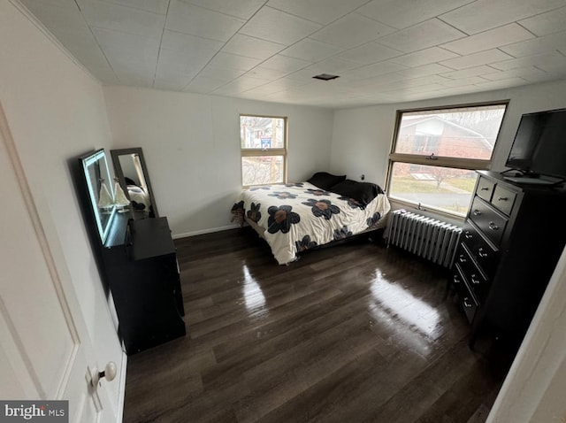 bedroom with multiple windows, radiator heating unit, and dark wood-type flooring