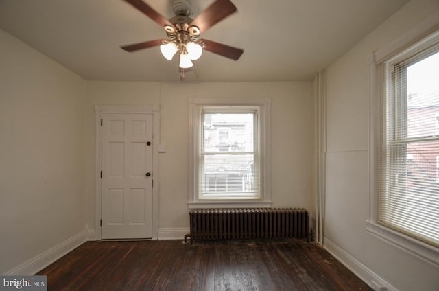 spare room featuring ceiling fan, radiator heating unit, dark wood-type flooring, and plenty of natural light