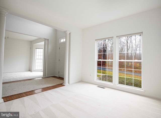 empty room featuring light wood-type flooring, a wealth of natural light, and decorative columns