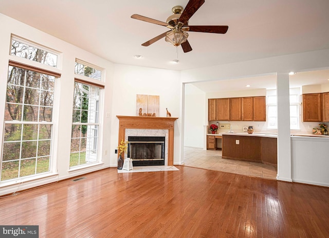 unfurnished living room with a high end fireplace, light hardwood / wood-style flooring, and ceiling fan