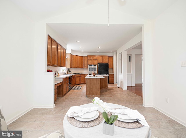 kitchen featuring a center island with sink, black refrigerator, stainless steel double oven, and vaulted ceiling