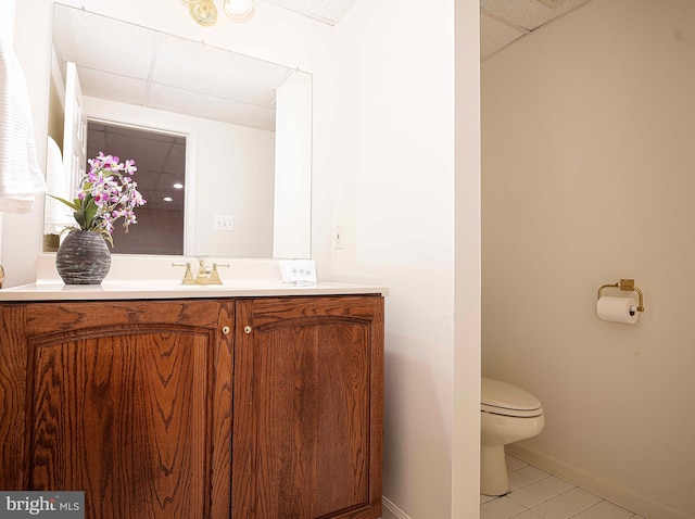 bathroom featuring tile patterned flooring, vanity, toilet, and a drop ceiling