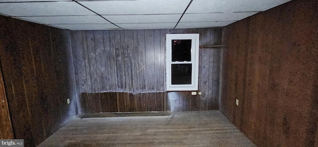 unfurnished room featuring wood walls and a drop ceiling