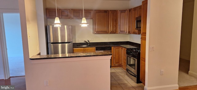 kitchen with dark stone counters, sink, hanging light fixtures, light tile patterned floors, and appliances with stainless steel finishes