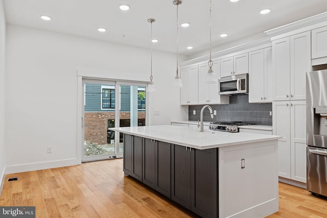 kitchen with a center island with sink, pendant lighting, white cabinets, and stainless steel appliances