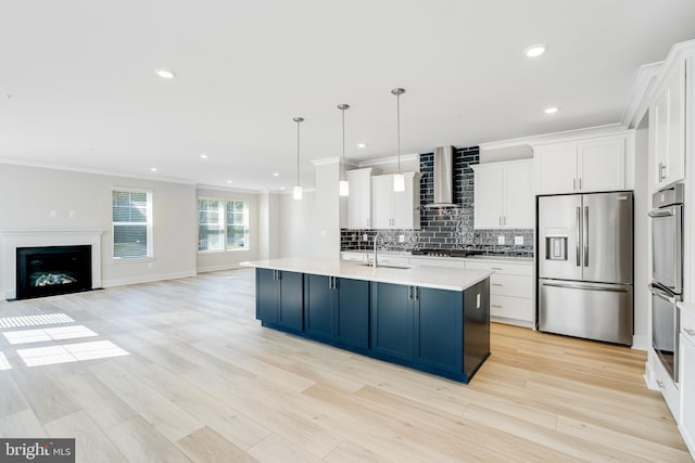 kitchen featuring a kitchen island with sink, white cabinets, wall chimney range hood, stainless steel refrigerator with ice dispenser, and decorative light fixtures