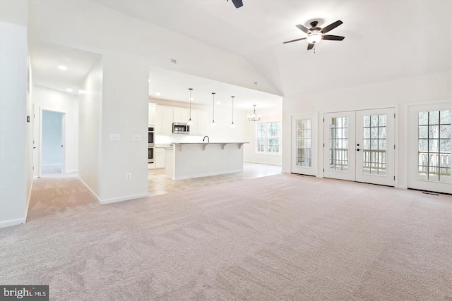 unfurnished living room with ceiling fan with notable chandelier, light colored carpet, a wealth of natural light, and french doors