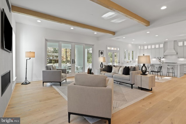 living room with a large fireplace, french doors, beamed ceiling, and light wood-type flooring