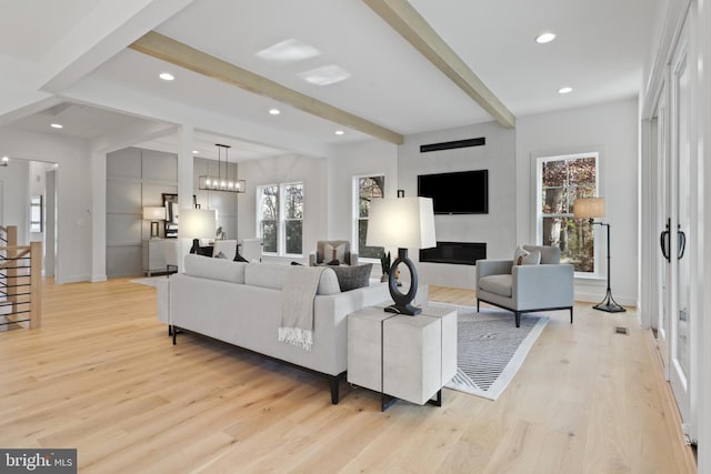 living room featuring beamed ceiling, light hardwood / wood-style floors, and an inviting chandelier