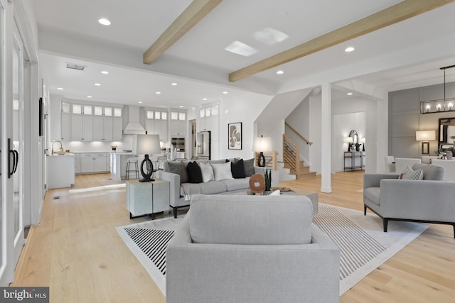 living room with beamed ceiling, a notable chandelier, and light wood-type flooring