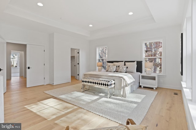 bedroom featuring light wood-type flooring, a tray ceiling, and multiple windows