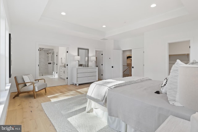 bedroom with ensuite bathroom, light hardwood / wood-style floors, a raised ceiling, and a closet