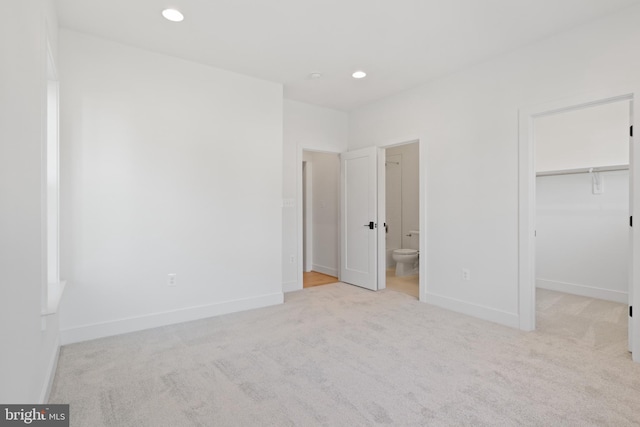 unfurnished bedroom with ensuite bathroom, a spacious closet, a closet, and light colored carpet