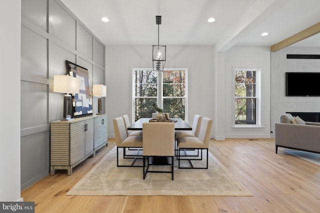 dining space featuring a large fireplace, beamed ceiling, light hardwood / wood-style floors, and an inviting chandelier