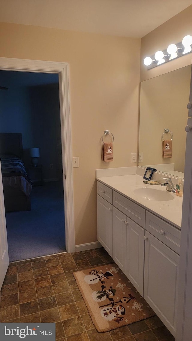 bathroom with ensuite bathroom, stone finish floor, vanity, and baseboards