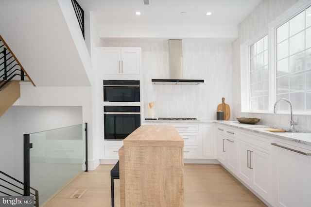 kitchen with white cabinetry, sink, wall chimney range hood, light hardwood / wood-style flooring, and decorative backsplash