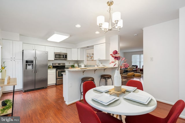 kitchen featuring white cabinets, dark wood-style floors, a peninsula, hanging light fixtures, and stainless steel appliances