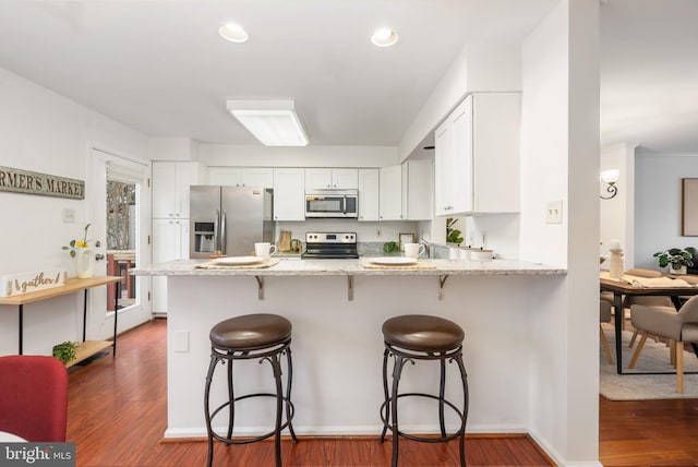 kitchen with a breakfast bar, stainless steel appliances, dark wood-type flooring, white cabinetry, and a peninsula