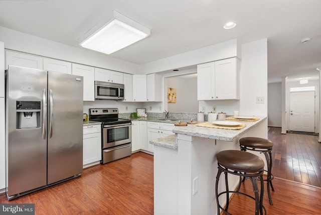 kitchen featuring a breakfast bar, wood finished floors, a peninsula, stainless steel appliances, and white cabinetry