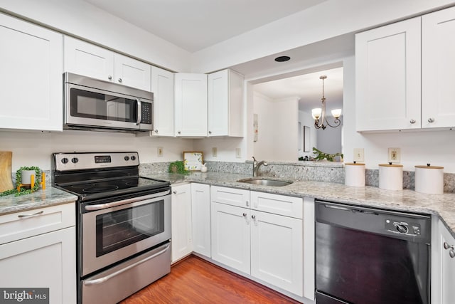 kitchen with appliances with stainless steel finishes, light stone countertops, light wood-type flooring, white cabinetry, and a sink