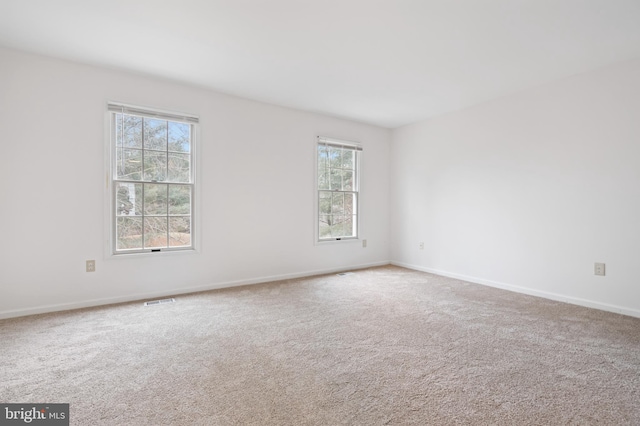 spare room with carpet floors, visible vents, and baseboards