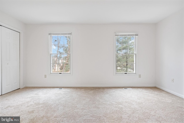 unfurnished bedroom featuring carpet floors, multiple windows, and visible vents