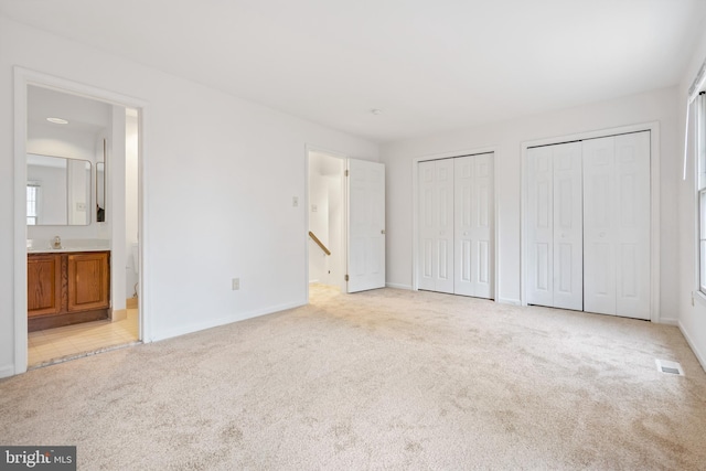 unfurnished bedroom with multiple closets, light carpet, baseboards, and ensuite bathroom