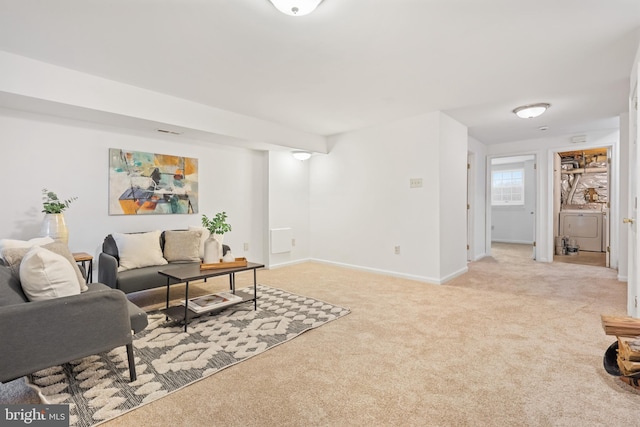 living room with baseboards, washer / clothes dryer, and light colored carpet