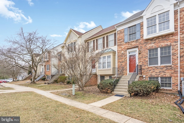 townhome / multi-family property featuring entry steps, a front yard, and brick siding