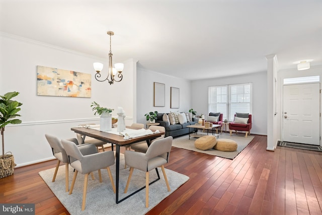 dining area with dark wood-type flooring, ornamental molding, baseboards, and an inviting chandelier