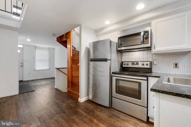 kitchen with backsplash, dark wood-type flooring, dark stone countertops, appliances with stainless steel finishes, and white cabinetry