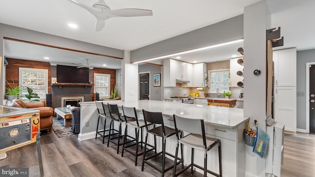 kitchen featuring kitchen peninsula, ceiling fan, dark wood-type flooring, white cabinets, and a breakfast bar area