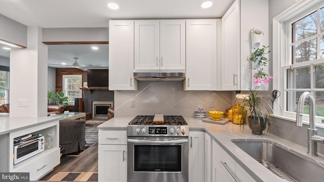 kitchen with a brick fireplace, white cabinetry, stainless steel gas range oven, and sink